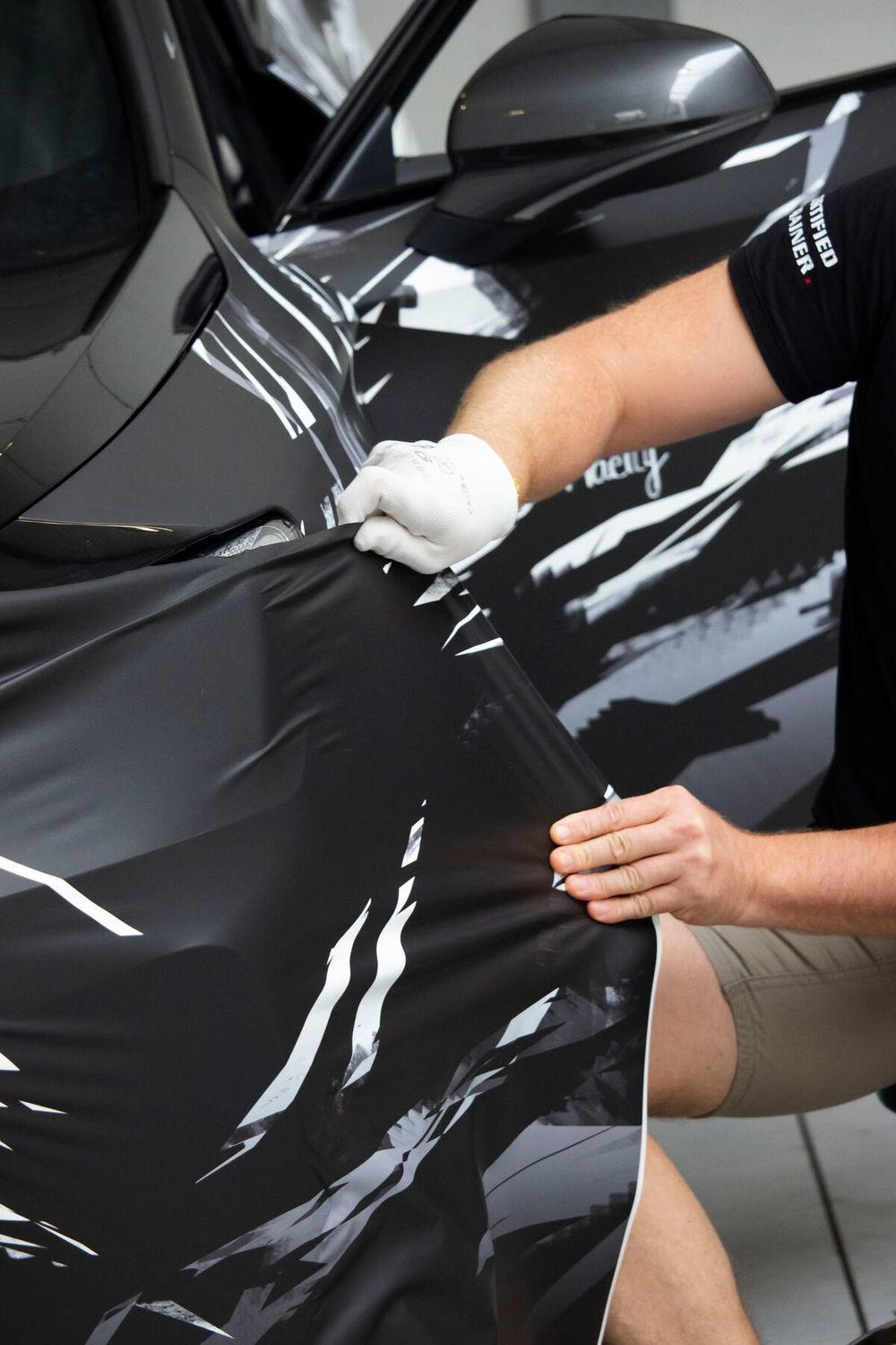 Gloved hands pulling black vinyl across a car panel
