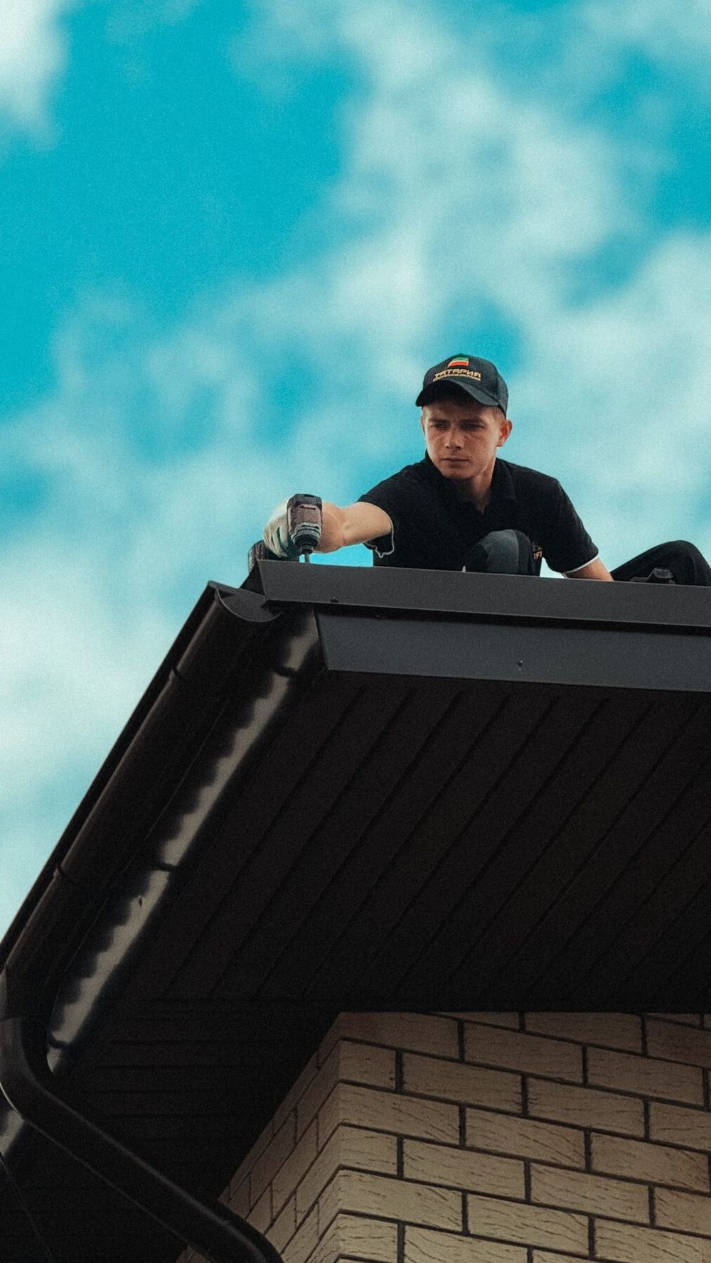 Roofer working on a dark roof against a blue sky