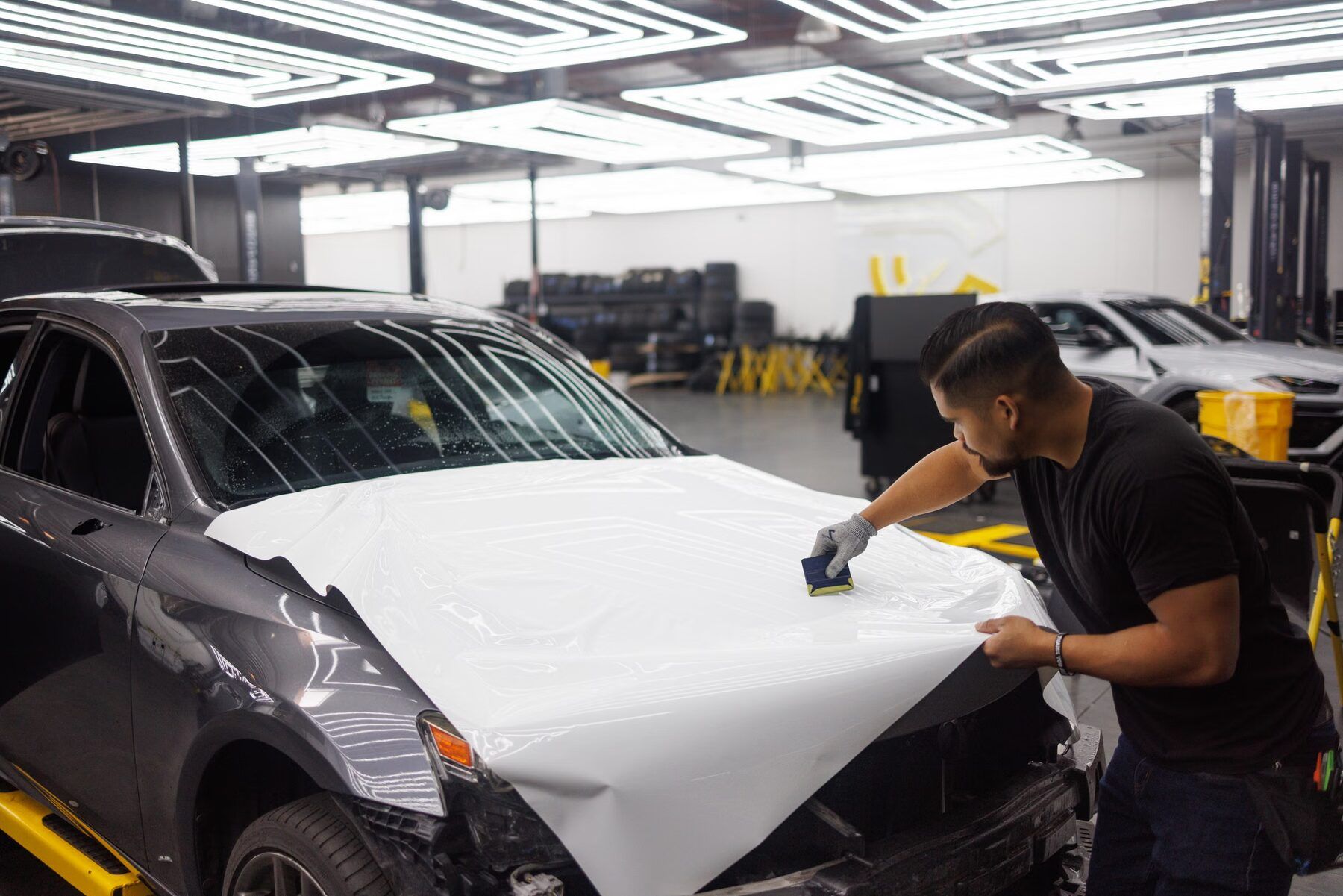 Installer wrapping a car in white vinyl inside a shop bay