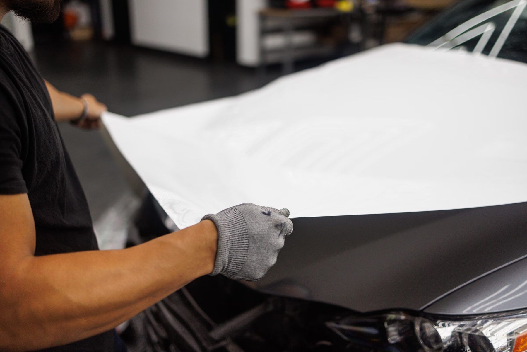 Installer’s hands laying white vinyl across a car hood