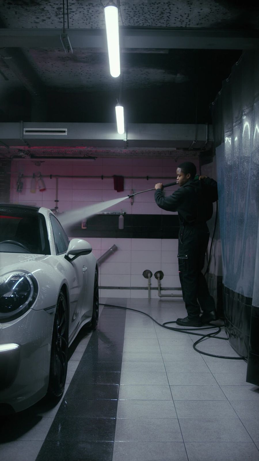Detailer rinsing a sports car in a shop bay