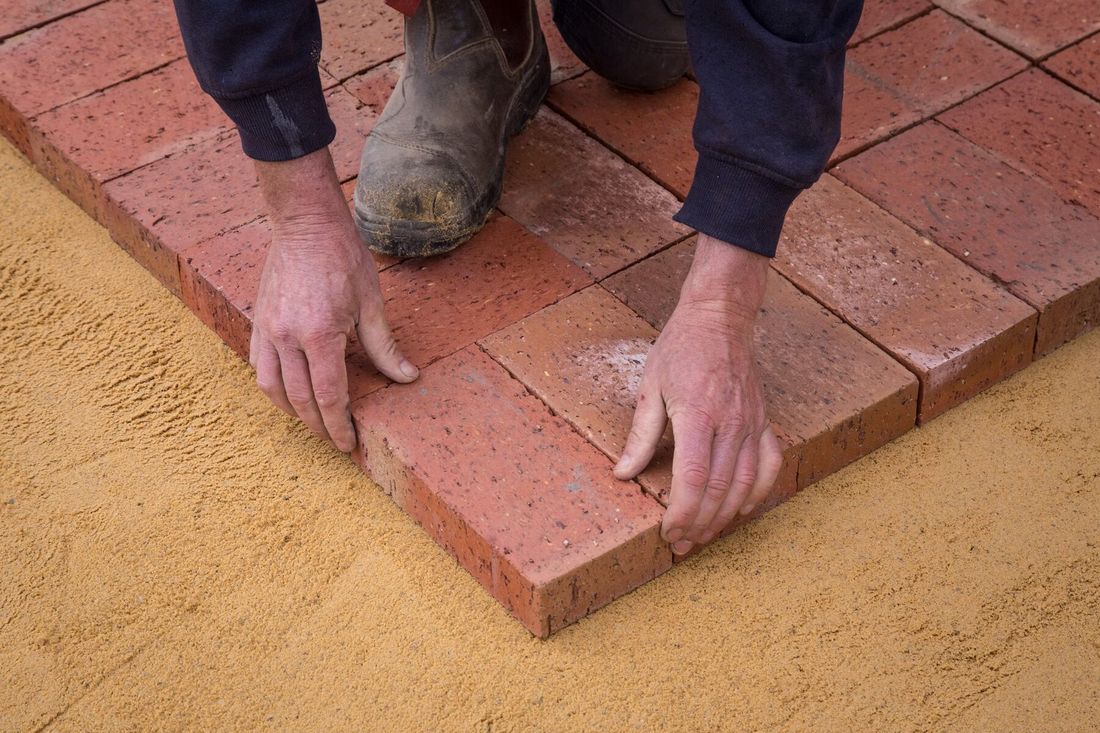 Hands setting red pavers into sand